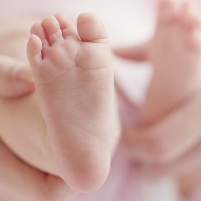Closeup of mother hands holding cute tiny baby feet, showing bab
